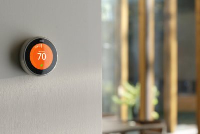 Orange smart thermostat mounted on wall displaying seventy degrees fahrenheit